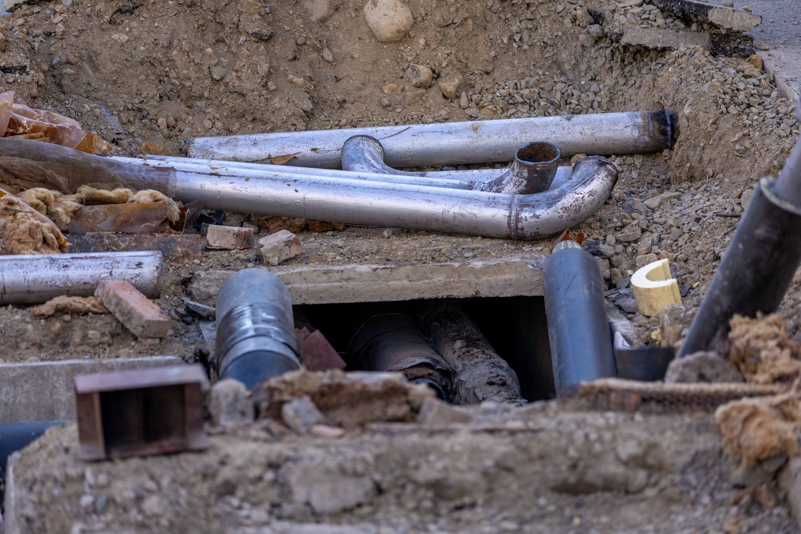 Wykop z odsłoniętymi stalowymi rurami, łukami i izolacją z wełny mineralnej oraz betonową płytą nad kanałem